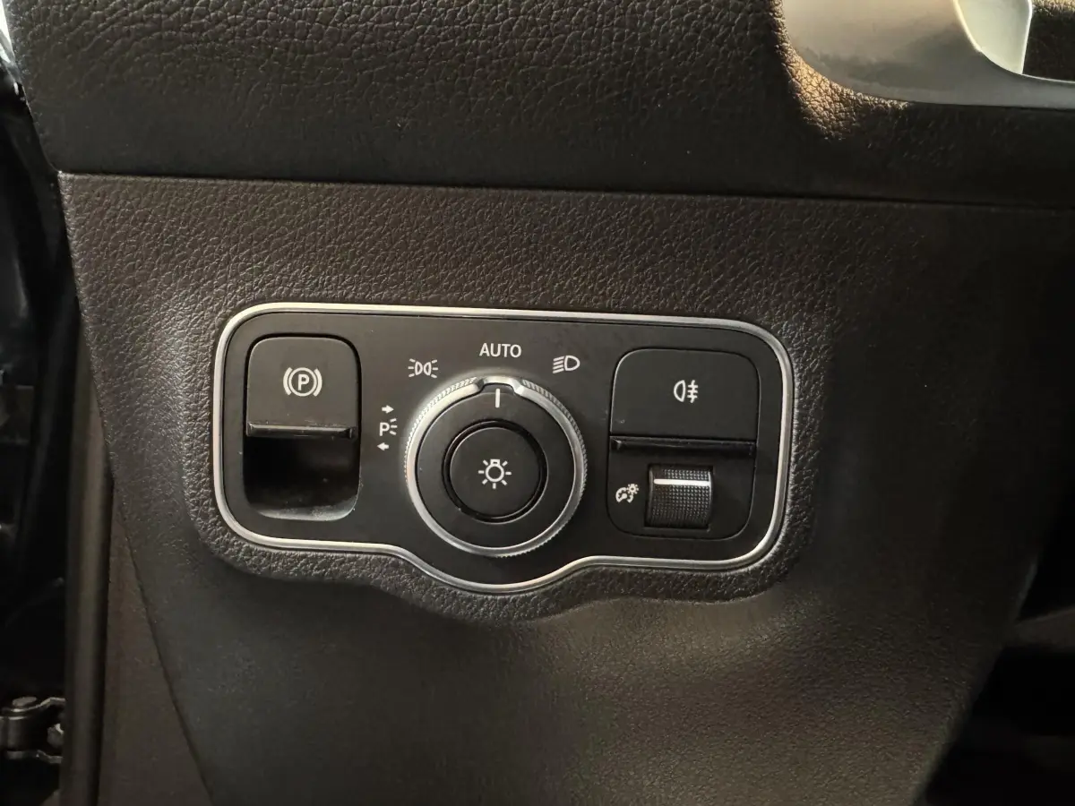 Gros plan sur le panneau de commande des phares et du frein à main électrique dans un Mercedes GLB 200 d AMG Line noir.