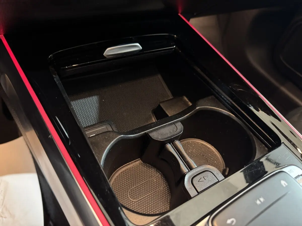 Gros plan sur la console centrale noire avec porte-gobelets et bande lumineuse rouge d’un Mercedes GLB 200 d AMG Line.