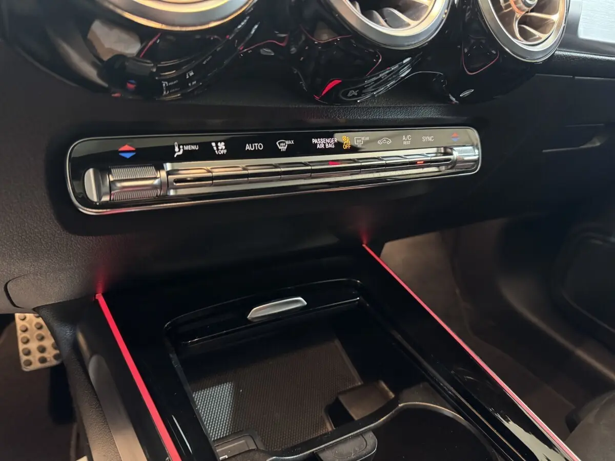 Vue rapprochée de la console centrale noire du Mercedes GLB 200 d AMG Line avec commandes climatisation et éclairage d’ambiance rouge.