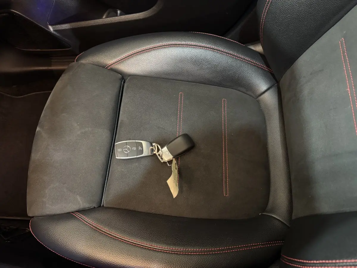 Gros plan sur la clé Mercedes posée sur un siège avant en cuir noir avec surpiqûres rouges du GLB 200 d AMG Line.