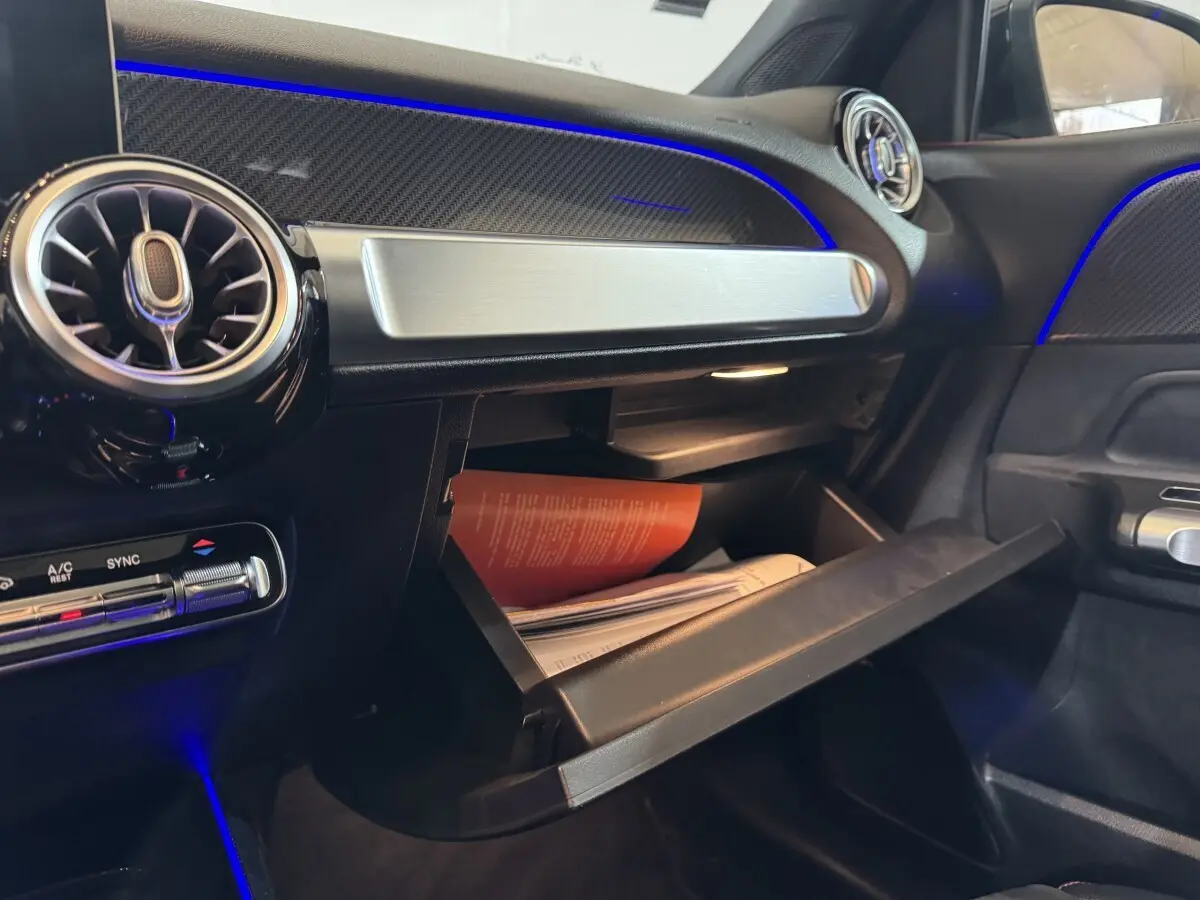 Intérieur du Mercedes GLB 200 d AMG Line noir, vue côté passager sur boîte à gants ouverte avec éclairage bleu d'ambiance.