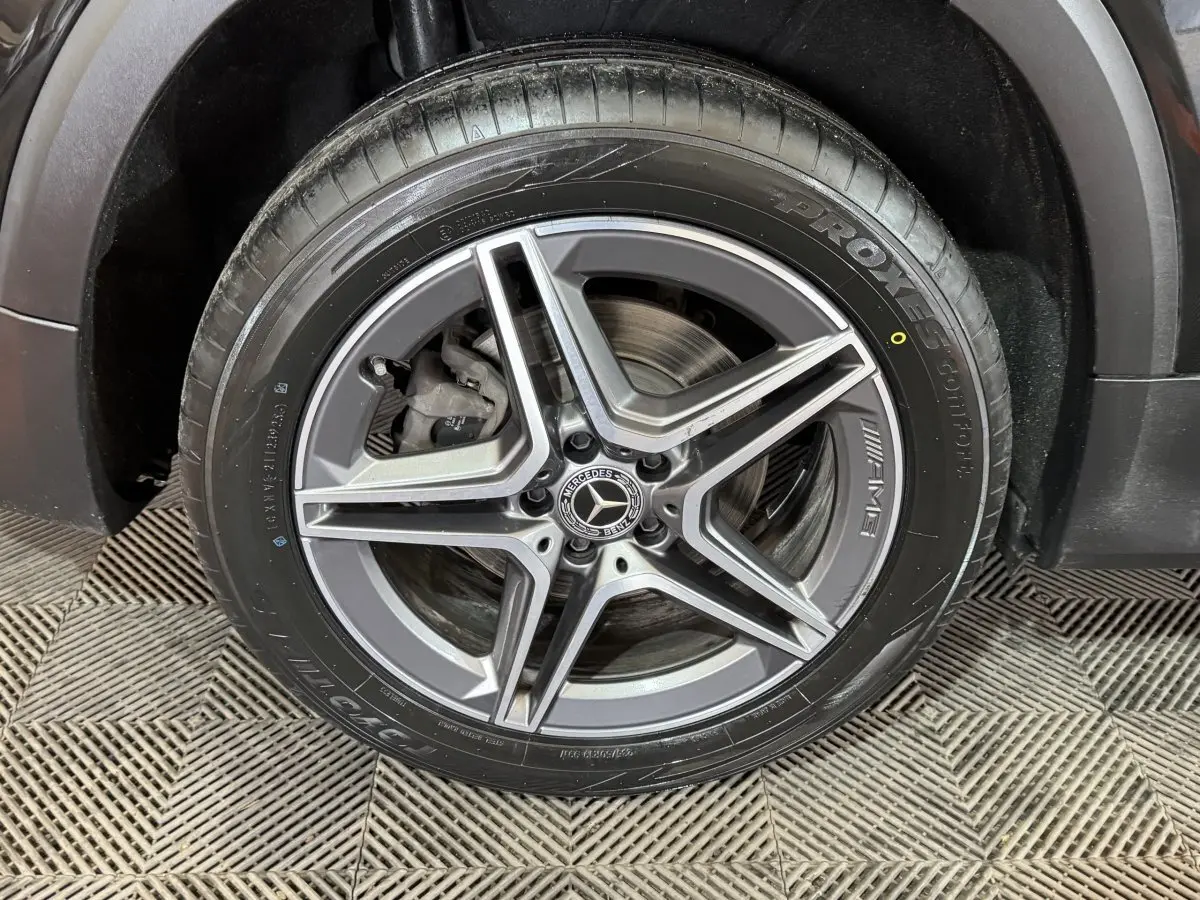 Gros plan sur la roue avant gauche noire du Mercedes GLB 200 d AMG Line avec jante AMG à cinq branches.