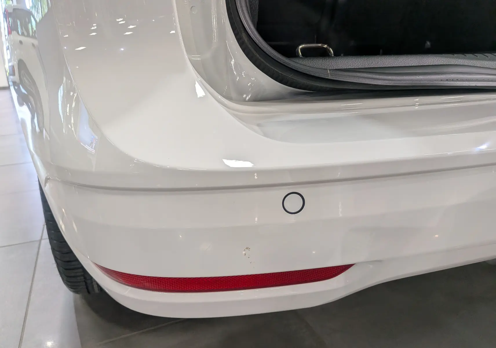 Gros plan sur le pare-chocs arrière blanc du Volkswagen Caddy 2.0 TDI avec capteur de recul et feu rouge intégré.