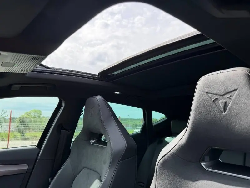 Vue intérieure avant du CUPRA Formentor bleu avec sièges sport en textile noir et toit ouvrant panoramique ouvert.