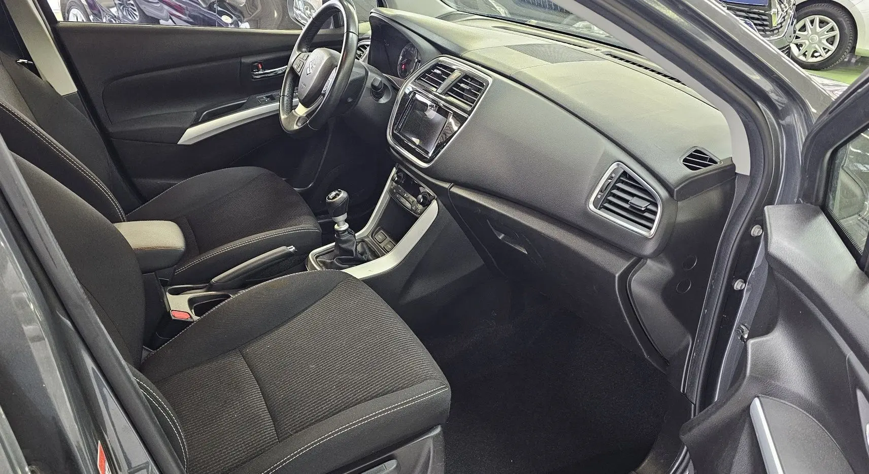 Intérieur avant du Suzuki SX4 S-Cross gris 2020, vue côté conducteur montrant sièges noirs et tableau de bord moderne.