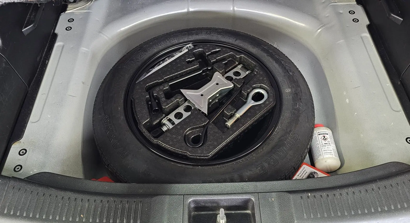 Gros plan sur la roue de secours et les outils de bord dans le coffre d'un Suzuki SX4 S-Cross gris 2020.