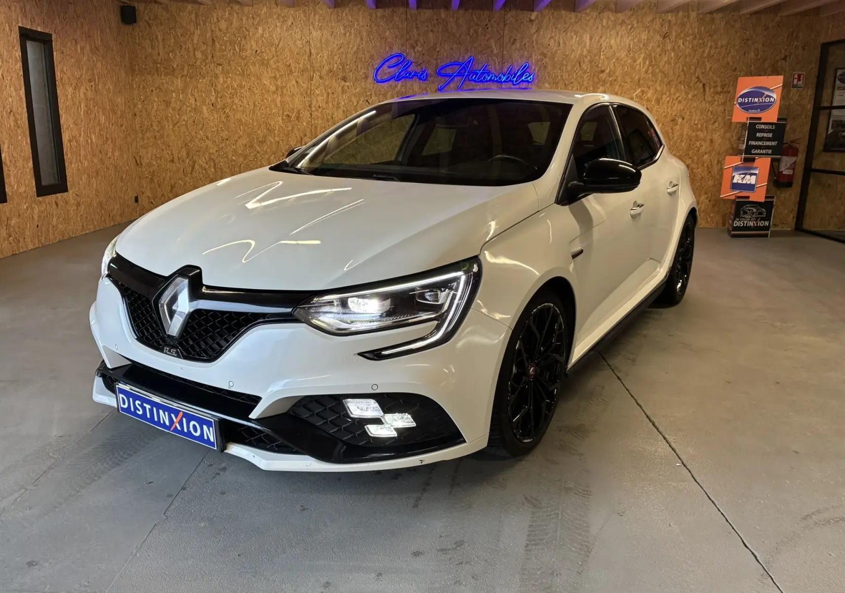 Renault Mégane IV RS 280 EDC6 blanche vue 3/4 avant droit, avec jantes noires et phares allumés en intérieur.