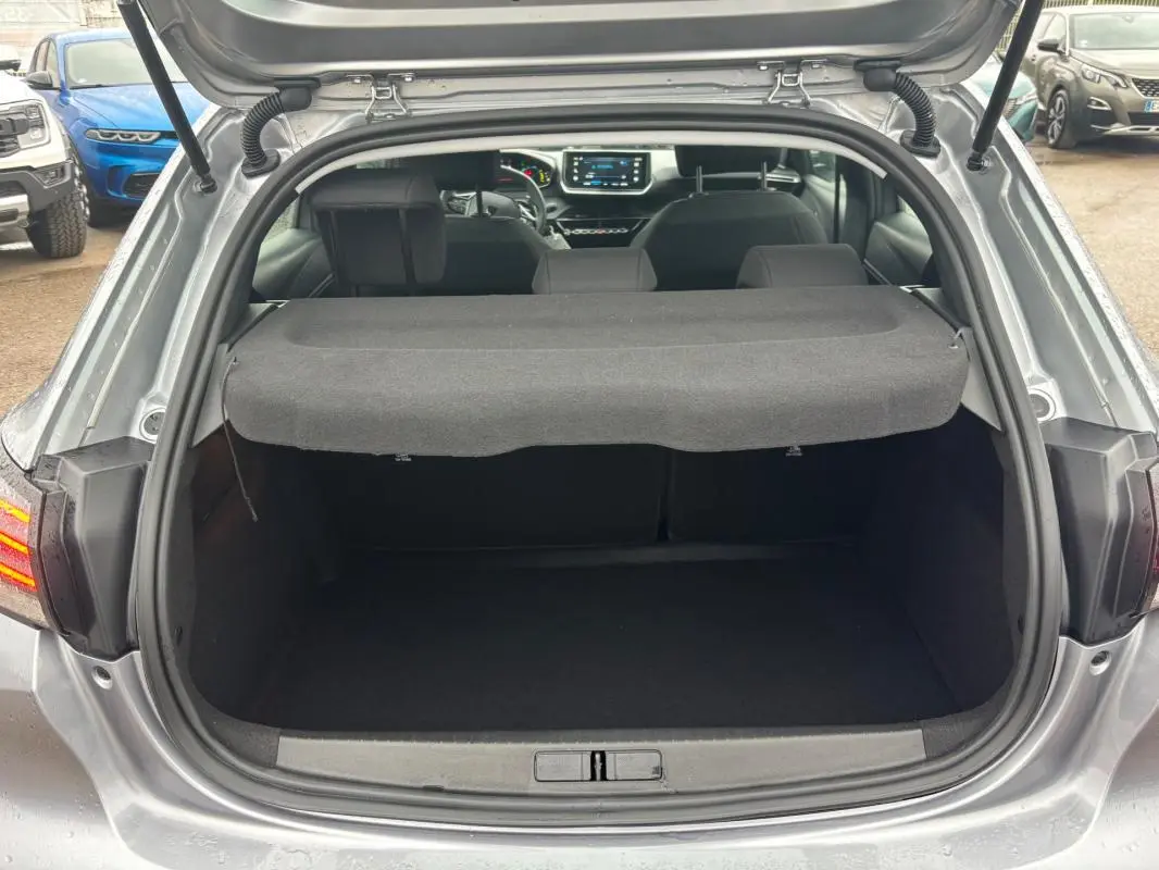 Vue arrière du coffre ouvert d'une Peugeot 208 Hybrid gris 2025, avec tablette cache-bagages et intérieur visible.