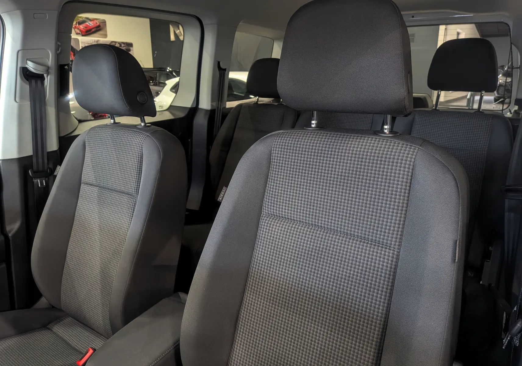 Vue intérieure sur les sièges avant en tissu gris du Volkswagen Caddy 2.0 TDI, avec banquette arrière visible en arrière-plan.