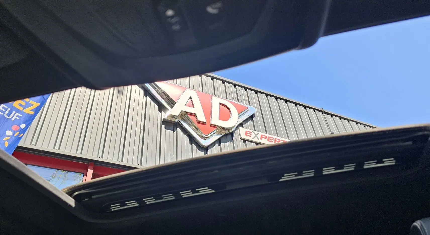 Toit ouvrant panoramique ouvert d'une BMW X4 xDrive20dA noire, vue vers le ciel et une enseigne AD Expert.