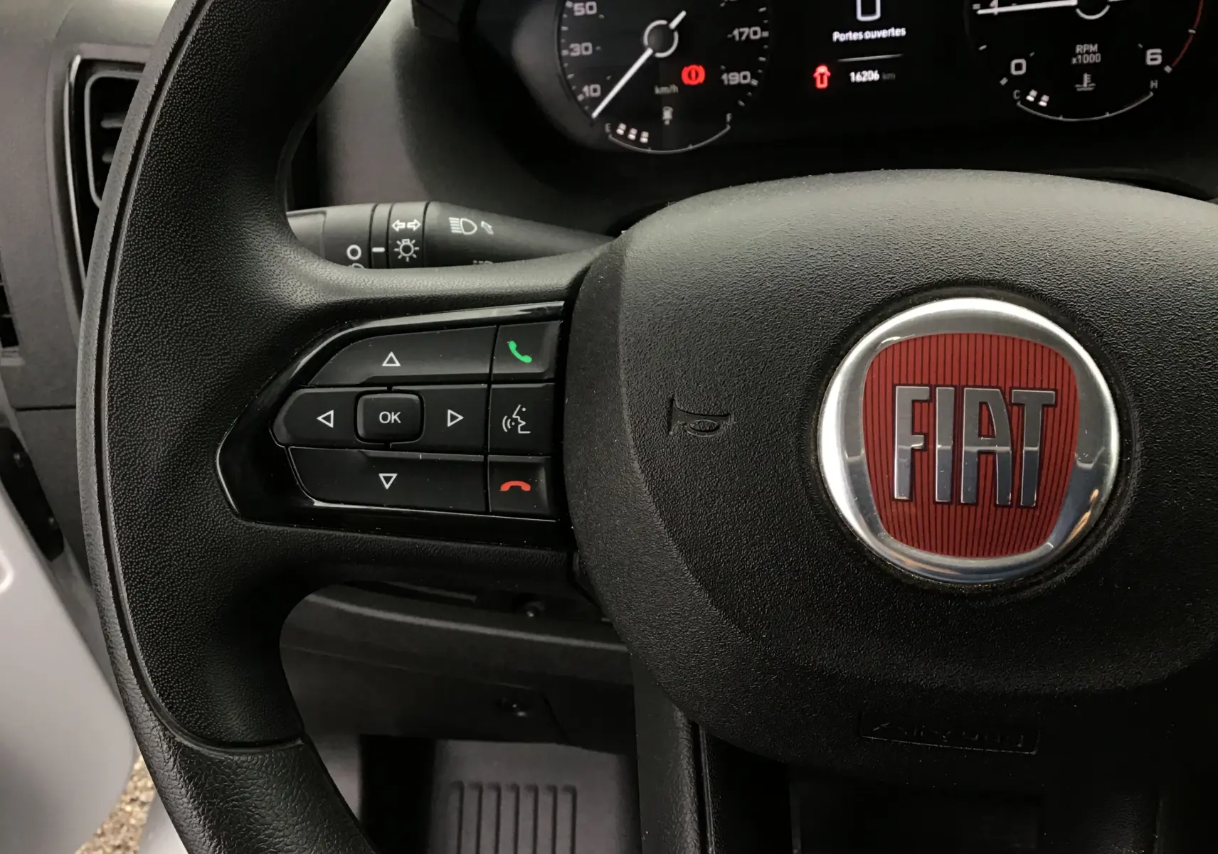 Gros plan sur le volant noir du Fiat Ducato Fourgon 2024 avec logo rouge et commandes intégrées côté gauche.