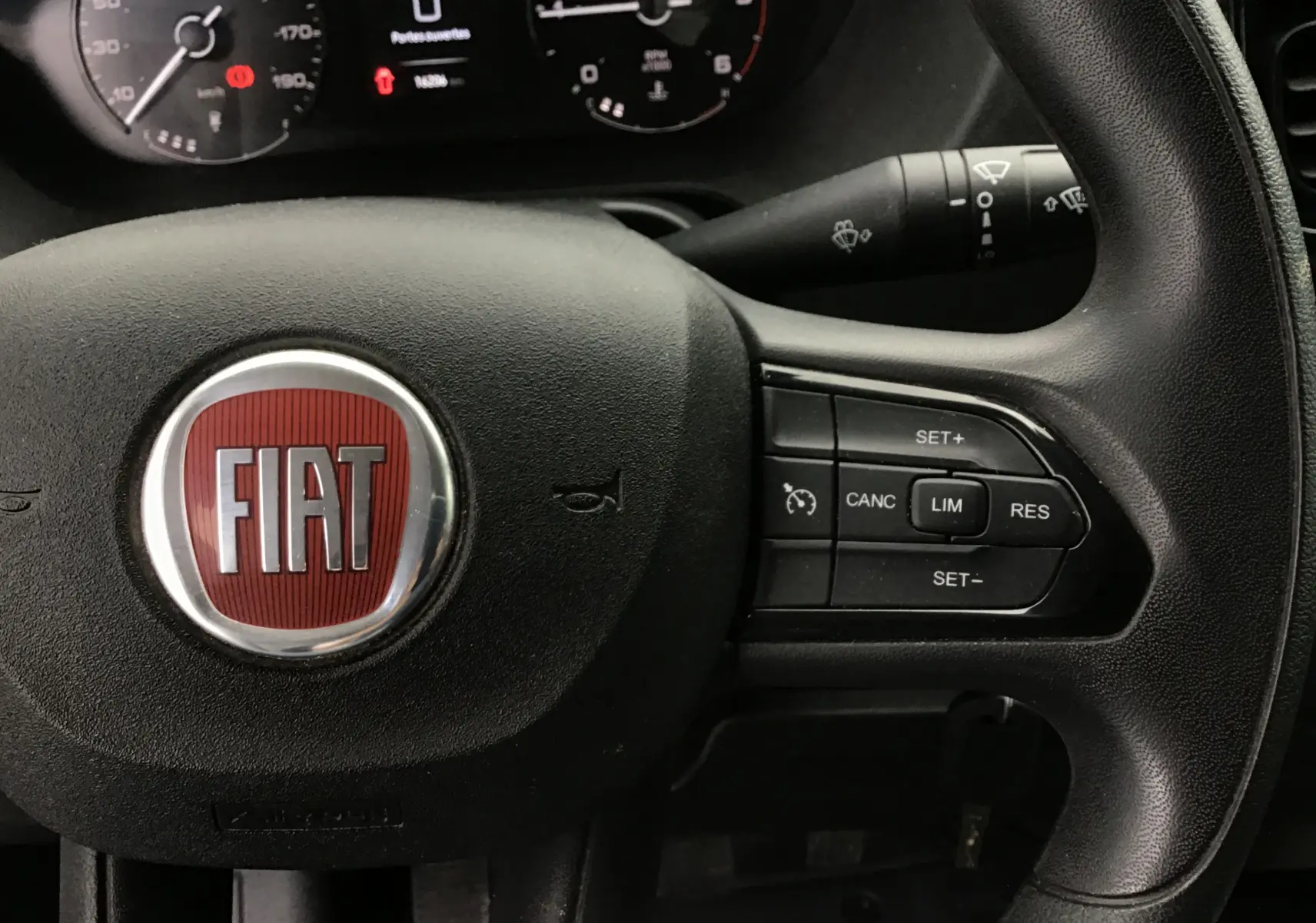 Gros plan sur le volant noir du Fiat Ducato Fourgon 2024 avec commandes de régulateur et logo rouge FIAT central.