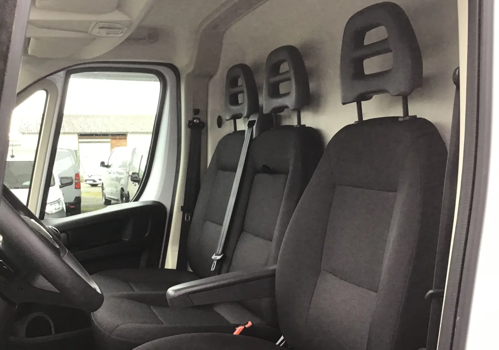 Vue intérieure côté conducteur du Fiat Ducato Fourgon blanc 2024, montrant les trois sièges noirs avec appuie-têtes.