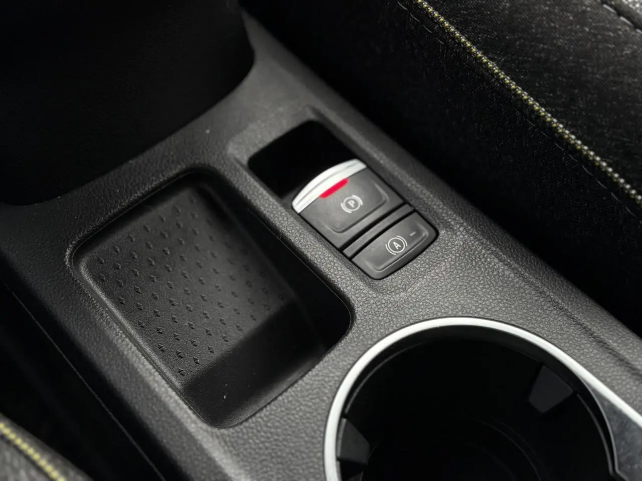 Gros plan sur la console centrale du Renault Captur 2025, montrant le frein à main électrique et un espace de rangement noir.