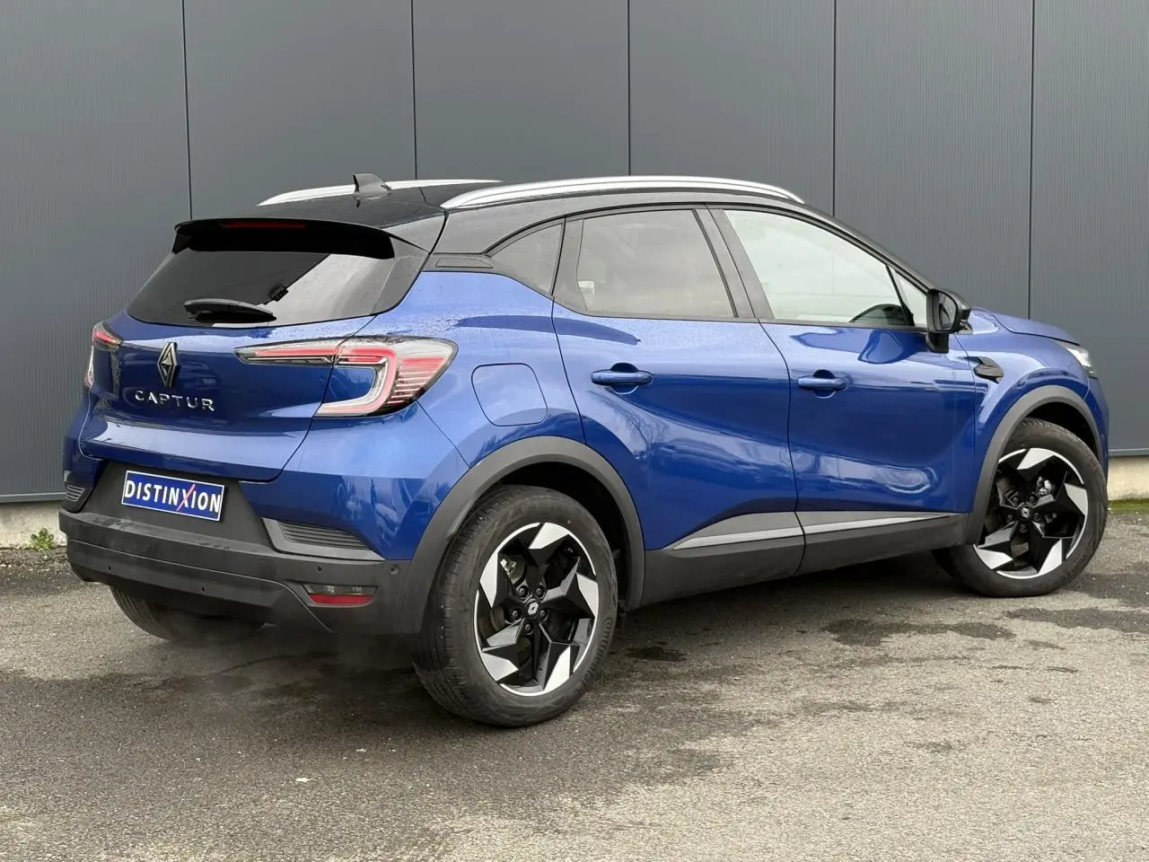 Vue 3/4 arrière droite du Renault Captur 2025 bleu Iron avec toit noir, jantes alu 18 pouces diamantées noires et railing de toit alu.