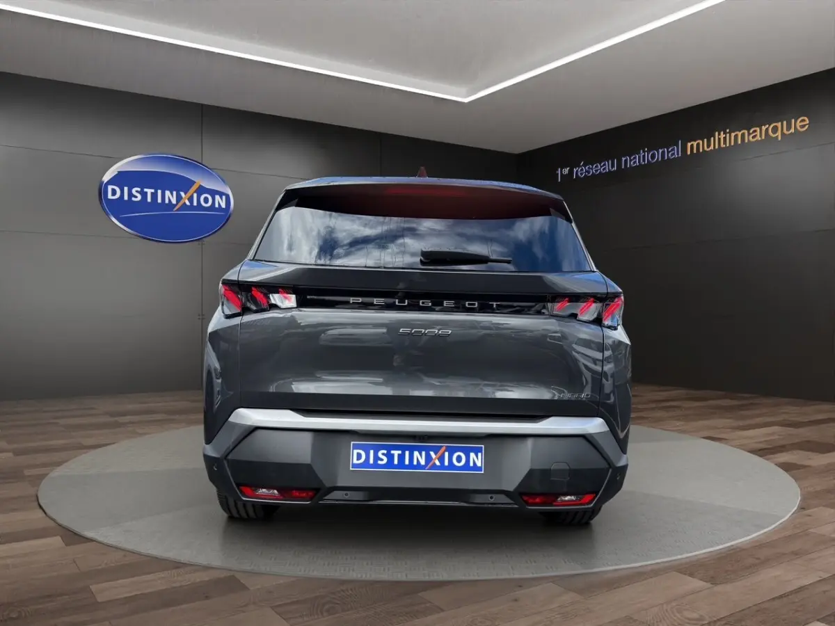 Vue arrière d'un Peugeot 5008 gris foncé hybride 2025 avec feux LED et logo distinctif sur fond showroom.