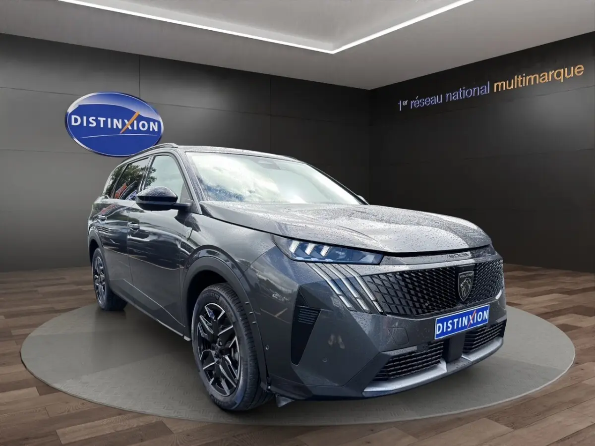 Peugeot 5008 gris foncé en 3/4 avant droit, avec calandre distinctive et jantes noires brillantes.