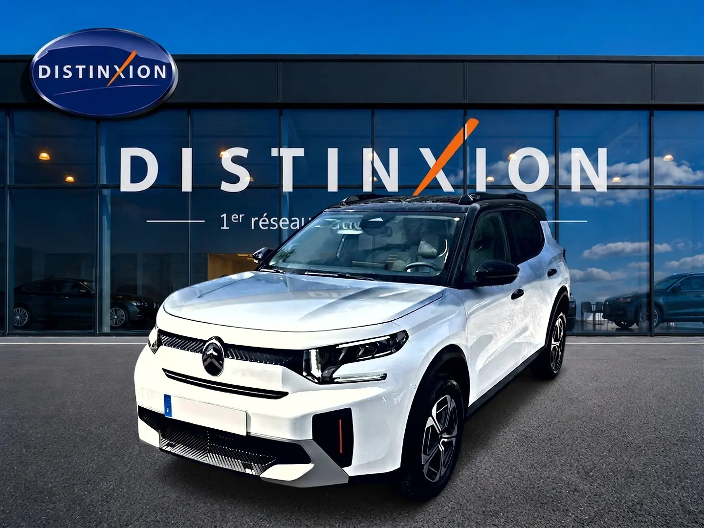 Citroën C3 Aircross blanc vue 3/4 avant droit, avec toit noir et jantes alu distinctives, devant vitrine Distinxion.