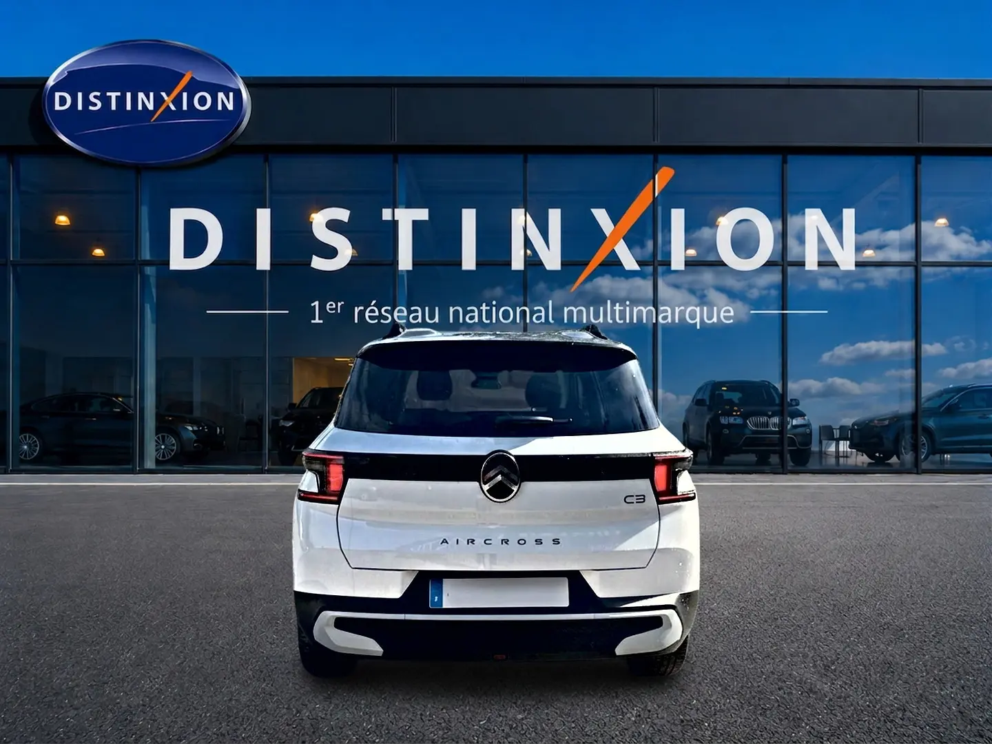 Vue arrière d'un Citroën C3 Aircross blanc garé devant une vitrine avec logo Distinxion visible.