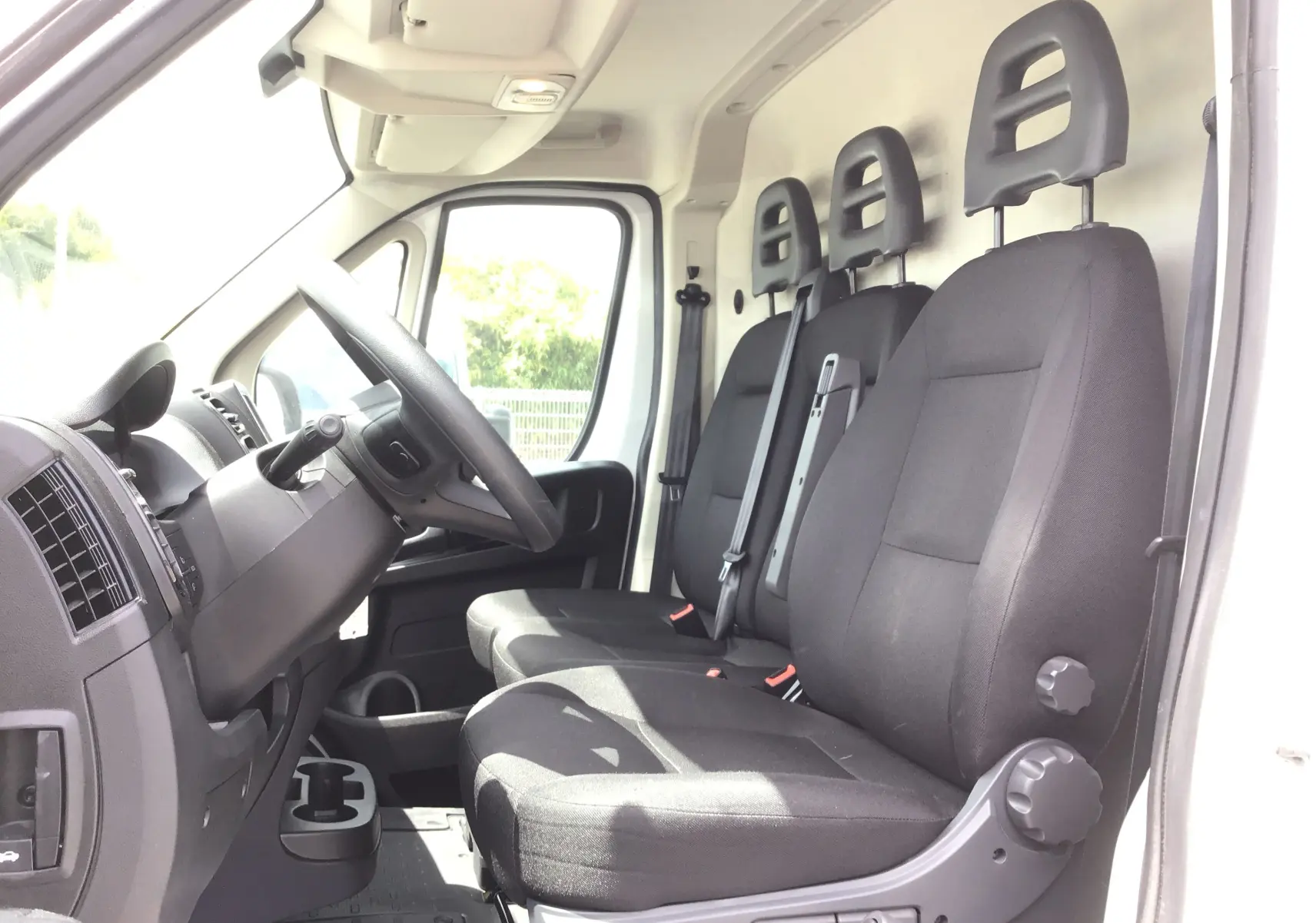 Vue intérieure côté conducteur du FIAT Ducato Fourgon blanc 2024, montrant les trois sièges noirs et le tableau de bord simple.
