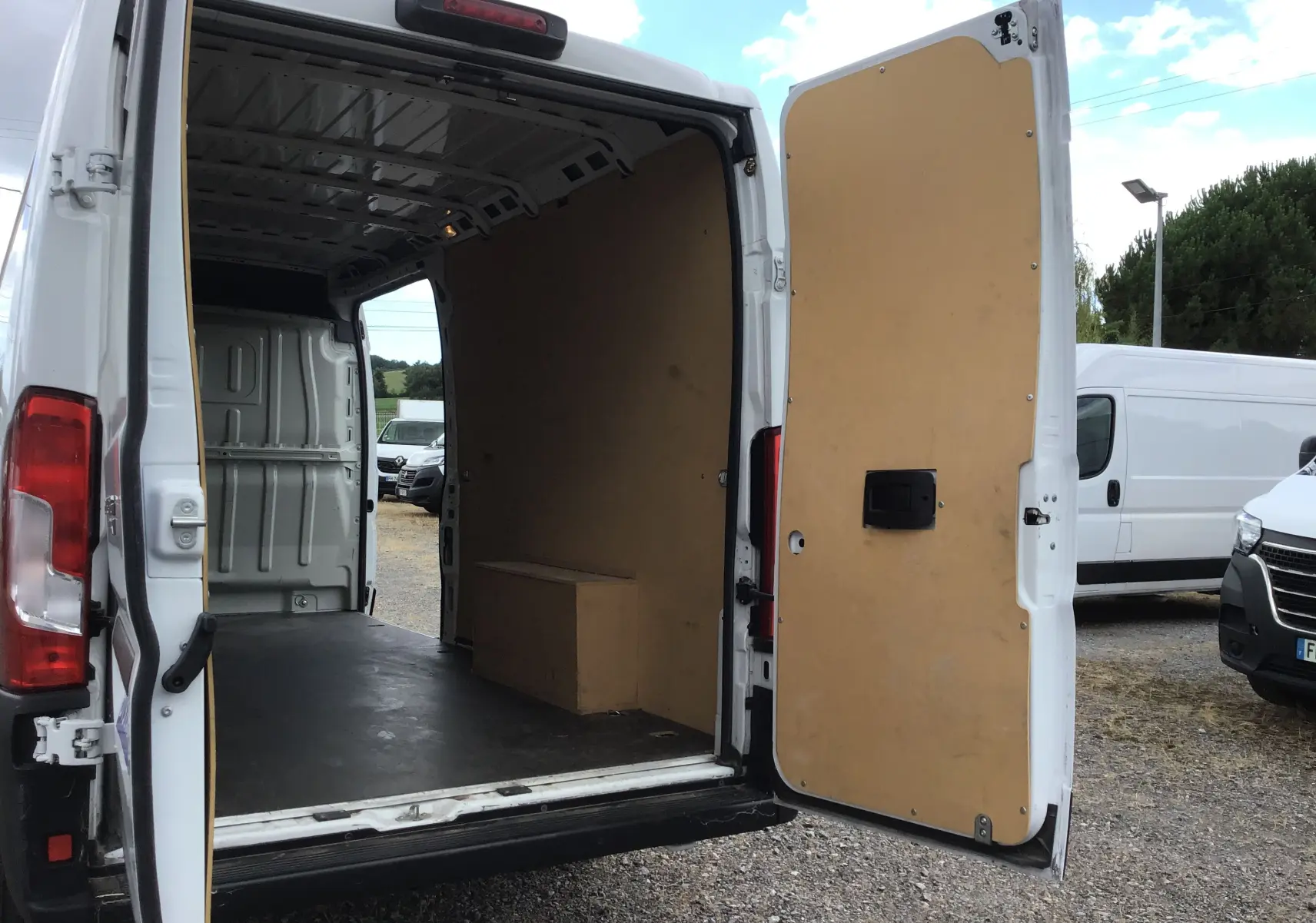 Vue arrière ouverte du FIAT Ducato Fourgon blanc 2024, montrant l'intérieur vide avec parois en bois et porte battante ouverte.