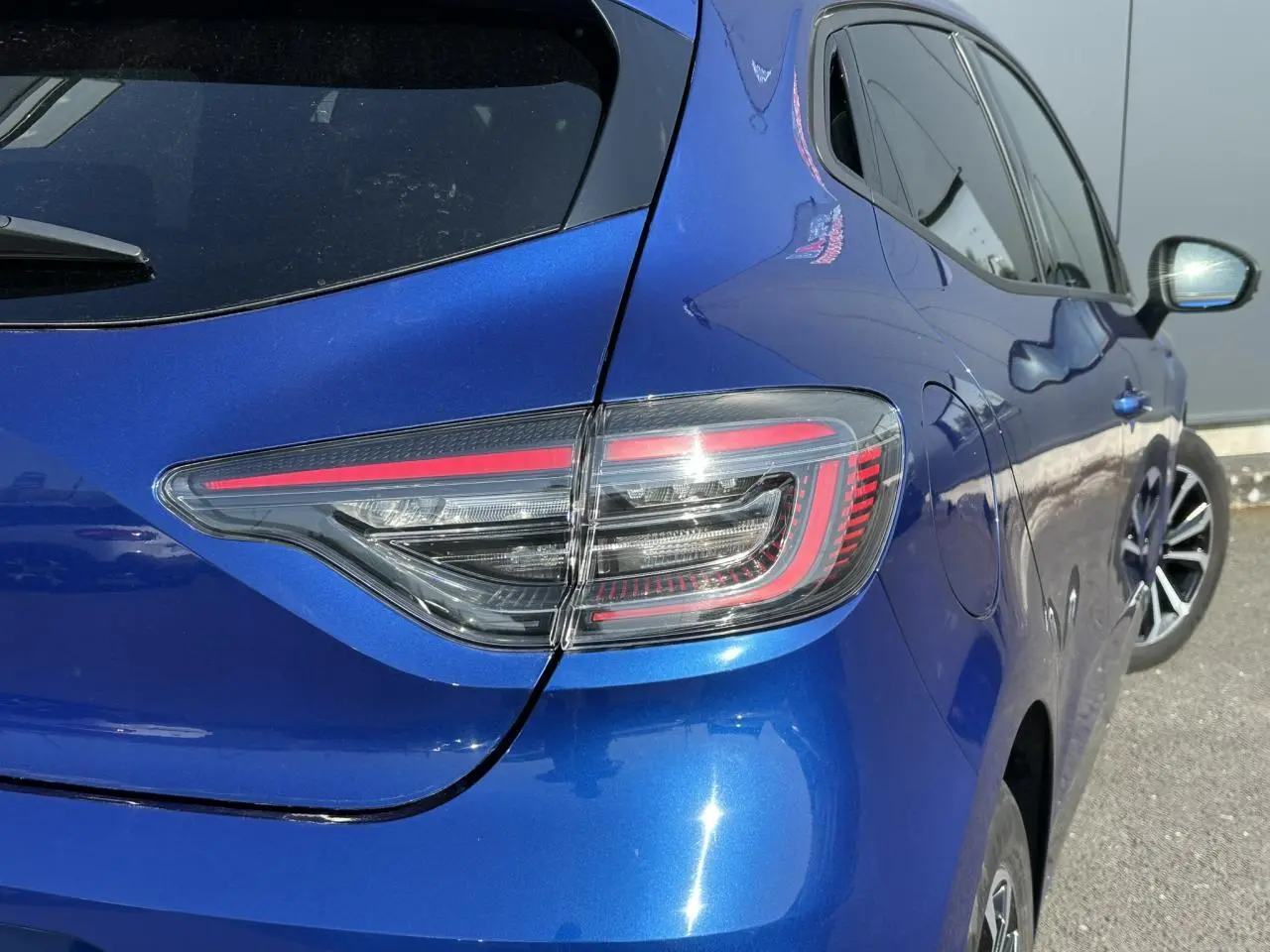 Feu arrière droit en gros plan sur Renault Clio 2025 Bleu Iron, avec reflet et partie latérale visible.