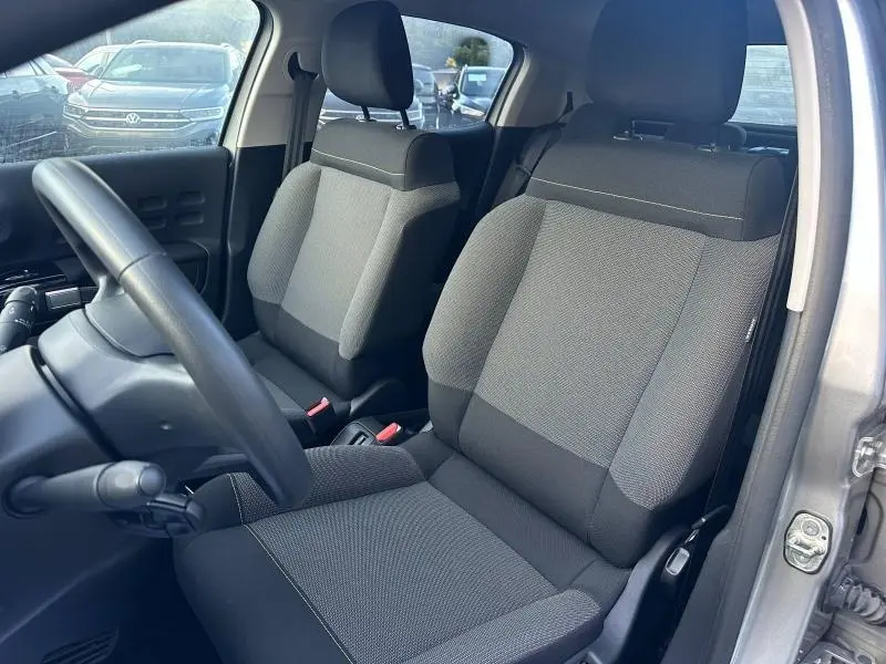 Vue intérieure côté conducteur de la Citroën C3 2023 gris, montrant les sièges avant en tissu et le volant.