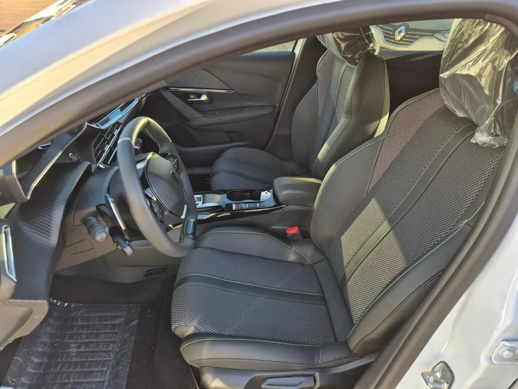 Vue intérieure côté conducteur de la Peugeot 208 Hybrid 136 GT blanche, avec sièges en tissu et volant multifonction.