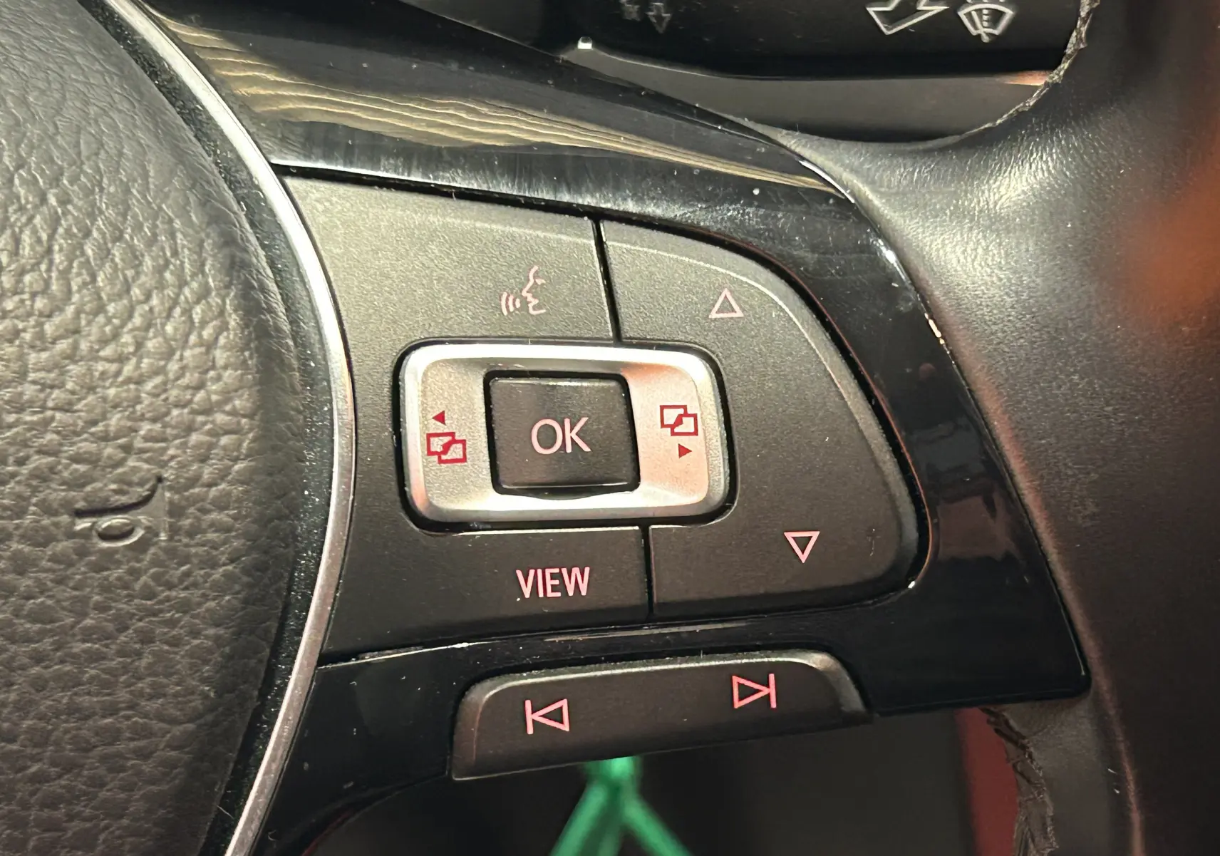 Gros plan sur les commandes du volant noir d’une Volkswagen Polo gris, boutons de navigation et fonction vocale visibles.