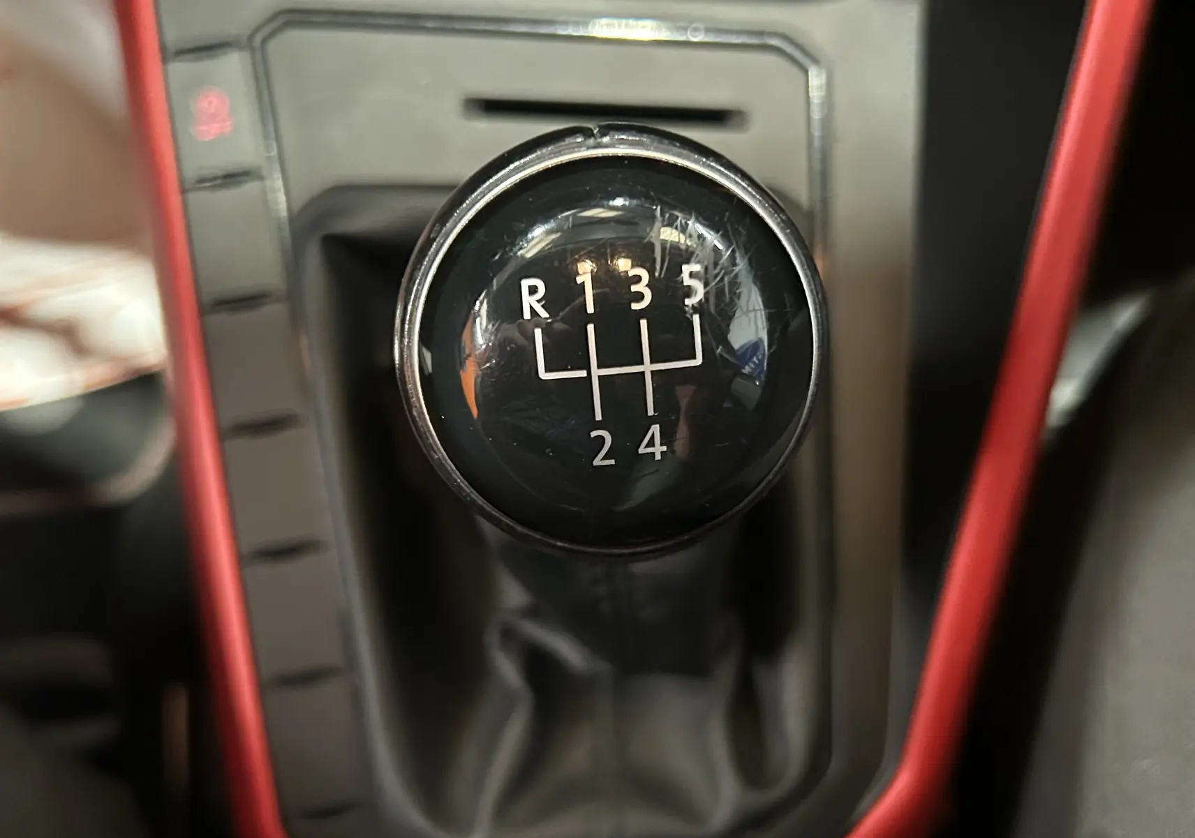 Gros plan sur le levier de vitesses manuel noir de la Volkswagen Polo gris, entouré d’un cadre intérieur rouge.