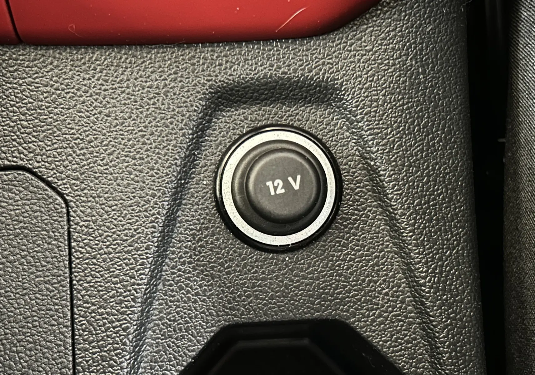 Gros plan sur la prise 12V intégrée dans la console centrale en plastique noir d’un Volkswagen Polo gris.