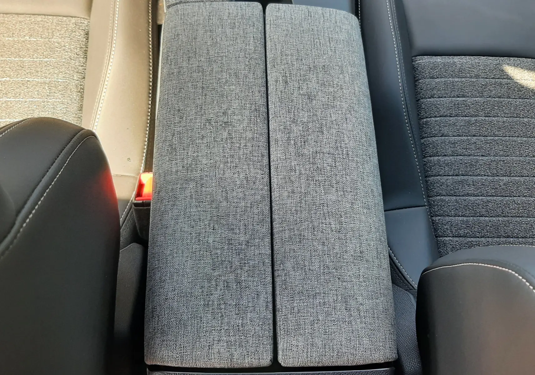 Vue plongeante sur l'accoudoir central gris tissu entre sièges avant noir et beige du Peugeot 5008 Hybrid 2025.