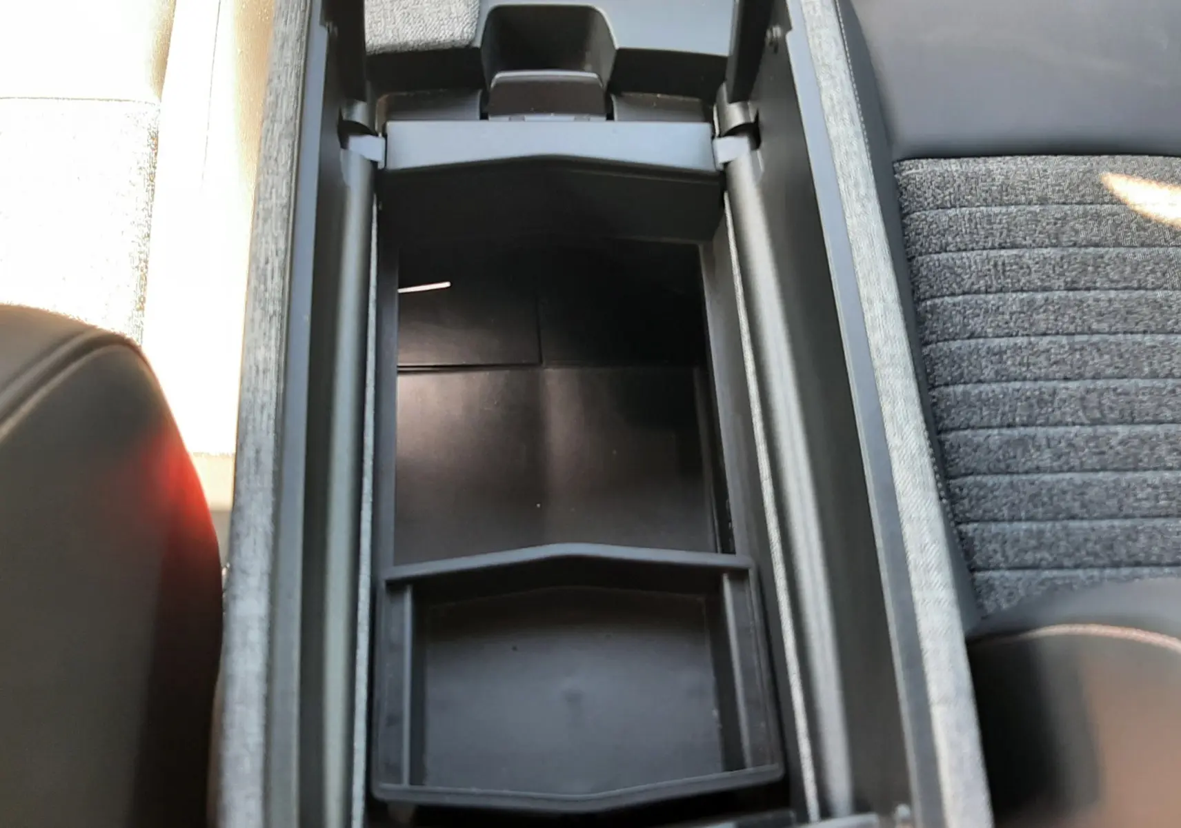 Vue plongeante sur le rangement central ouvert du Peugeot 5008 Hybrid 2025, avec console noire et sièges tissu gris.
