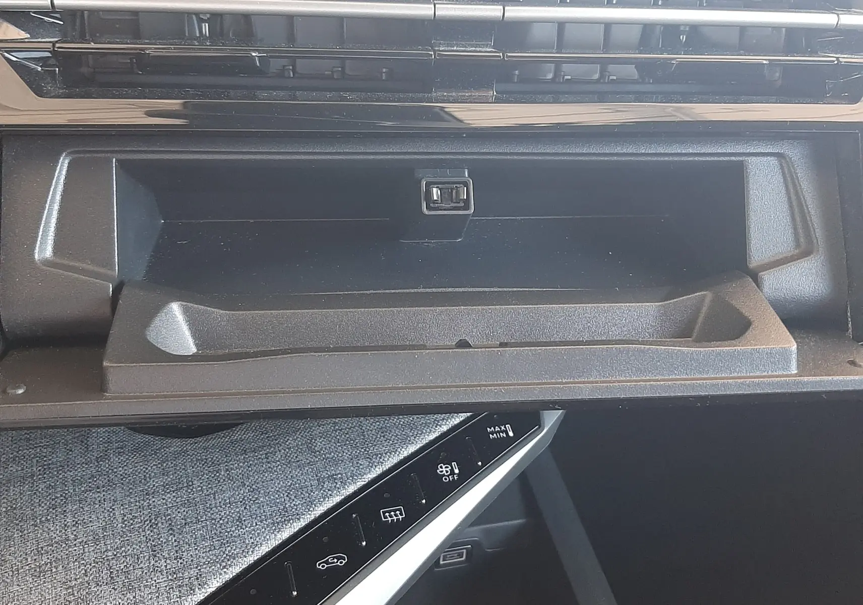 Gros plan intérieur sur la boîte à gants ouverte et la console centrale noire du Peugeot 5008 Hybrid blanc Okenite.