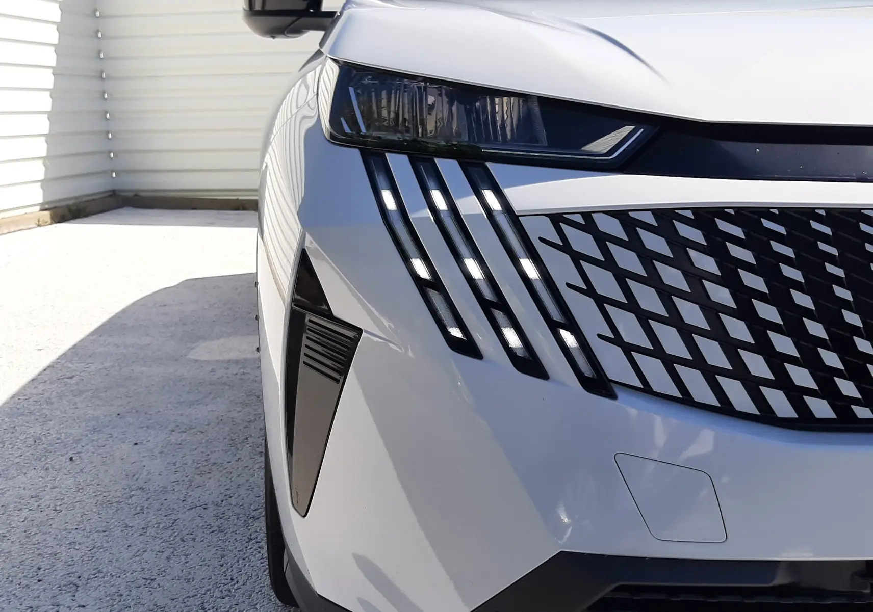 Gros plan sur l’avant droit blanc Okenite du Peugeot 5008 Hybrid 145ch, mettant en valeur ses phares LED et sa calandre distinctive.