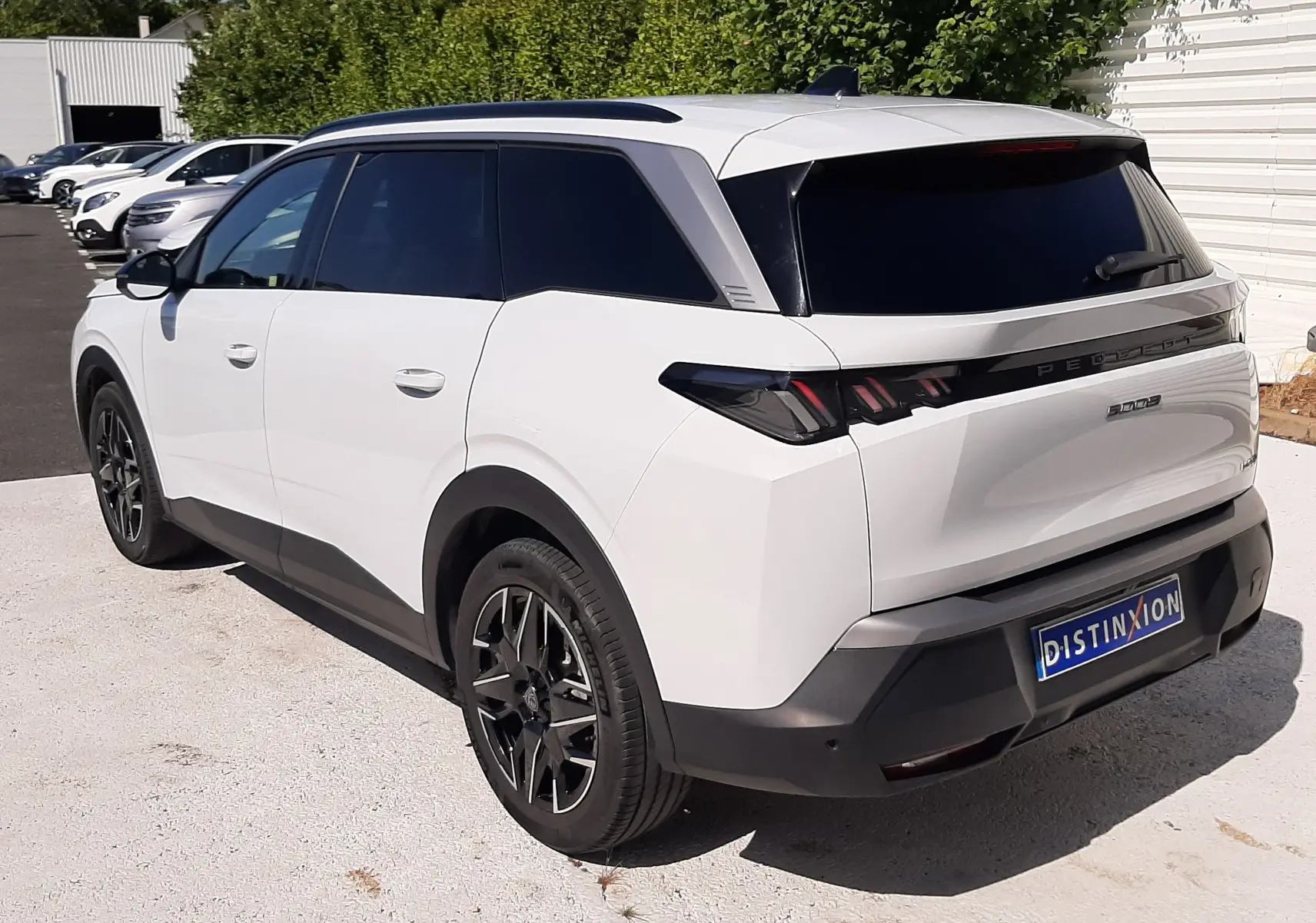 Vue 3/4 arrière droite du Peugeot 5008 blanc Okenite avec jantes noires et vitres teintées, stationné en extérieur.