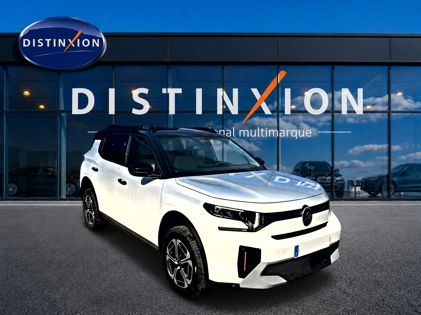 Vue 3/4 avant droite d'un Citroën C3 Aircross blanc avec toit noir et jantes alu devant une vitrine Distinxion.
