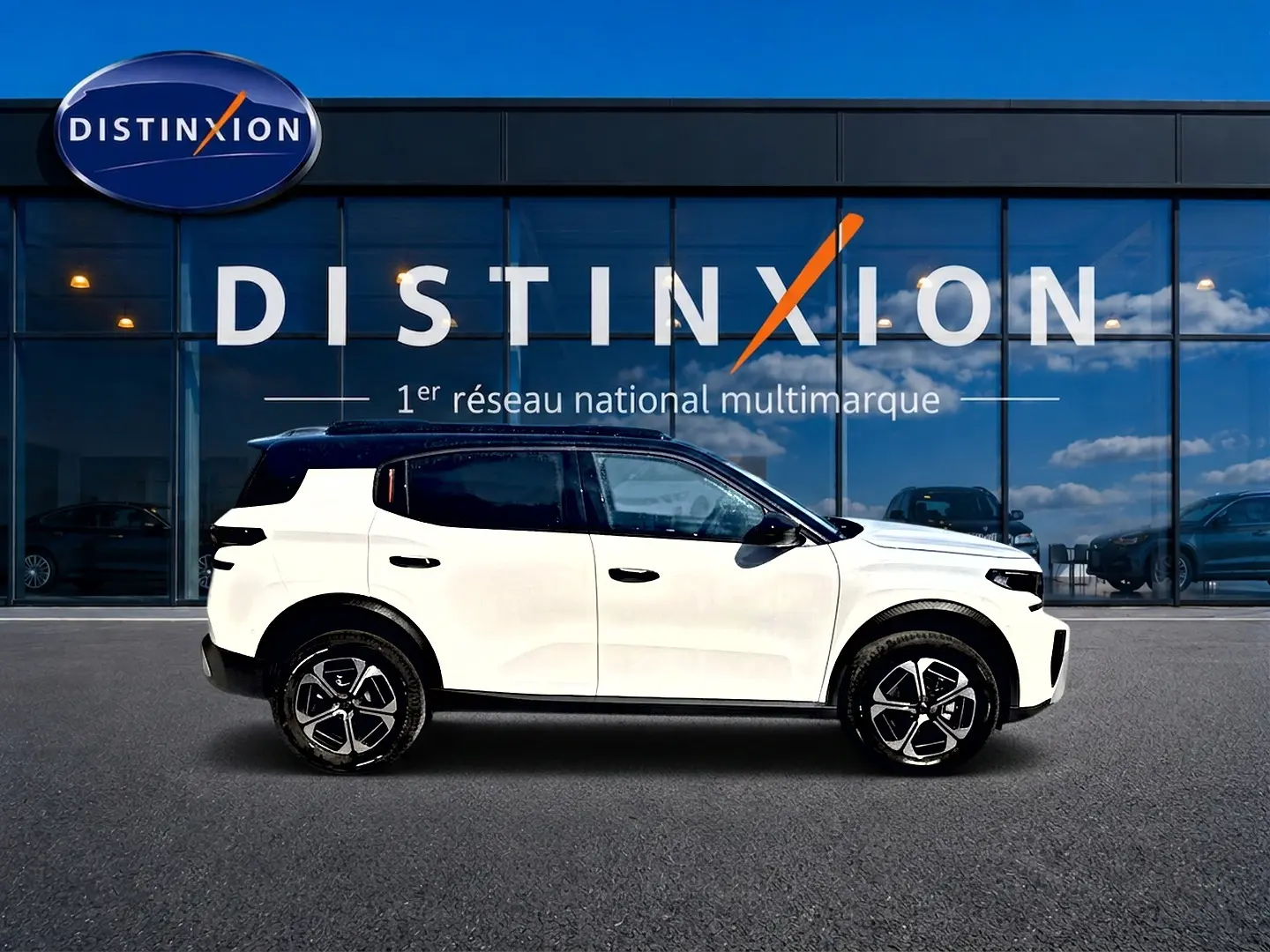 Profil droit d'un Citroën C3 Aircross blanc avec toit noir, jantes alu et vitres teintées devant une vitrine Distinxion.
