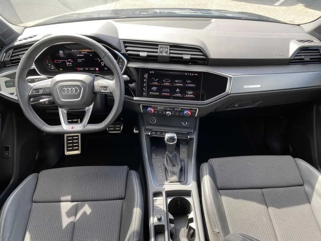 Vue intérieure avant de l'Audi Q3 2024 avec tableau de bord noir, volant cuir S line et console centrale moderne.