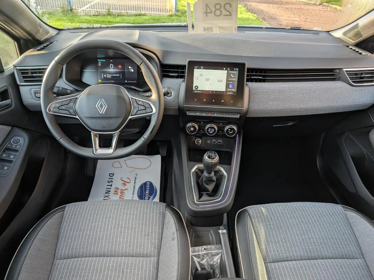 Vue intérieure avant de la Renault Clio 2025, tableau de bord gris avec volant multifonction et levier de vitesses manuel.