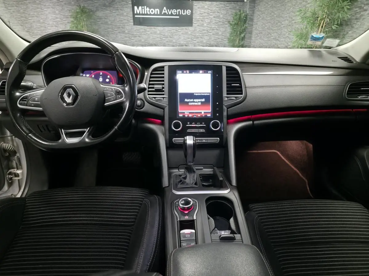 Intérieur avant d'une Renault Talisman Estate gris, tableau de bord noir avec éclairage d'ambiance rouge et écran tactile central.