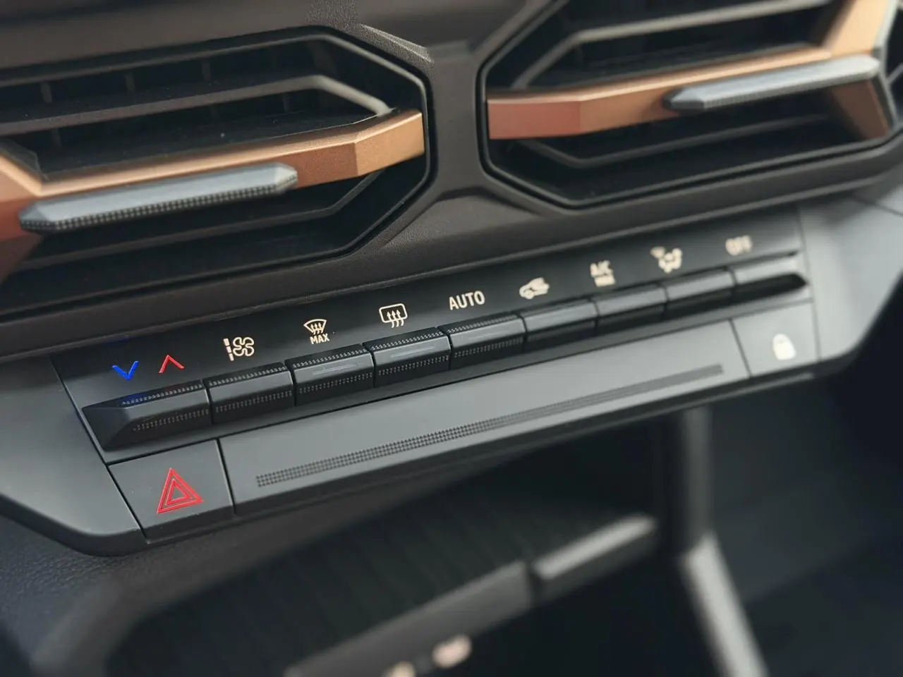Gros plan sur les commandes de climatisation et les aérateurs avec inserts cuivrés du Dacia Duster Beige Sandstone 2025.