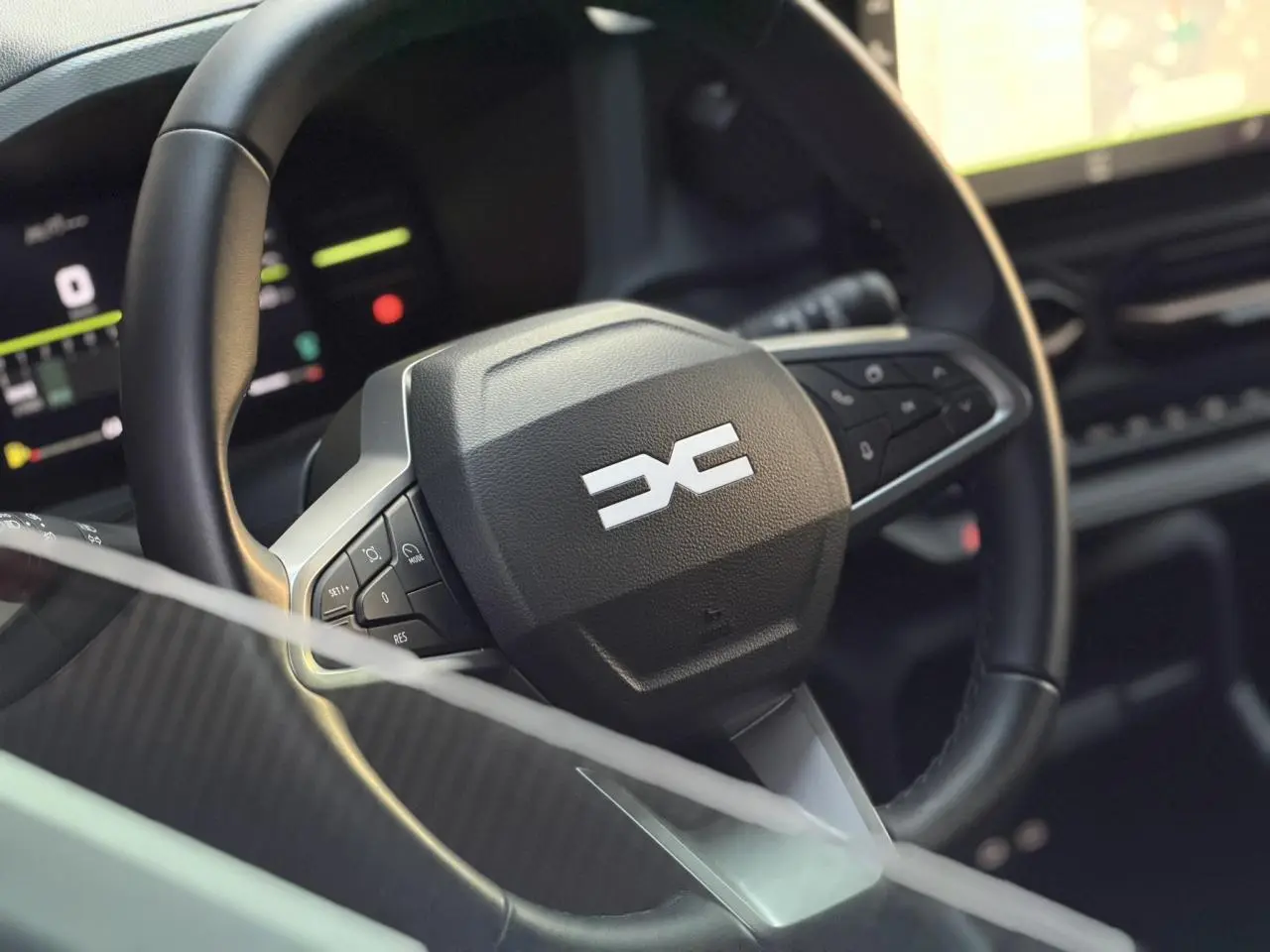 Gros plan sur le volant noir avec logo Dacia stylisé, tableau de bord digital en arrière-plan flou.