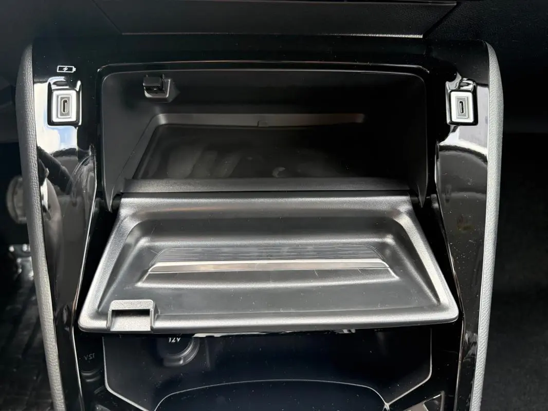 Gros plan intérieur sur le rangement central ouvert de la Peugeot 208 Hybrid 145 gris avec prise USB et finition noire brillante.