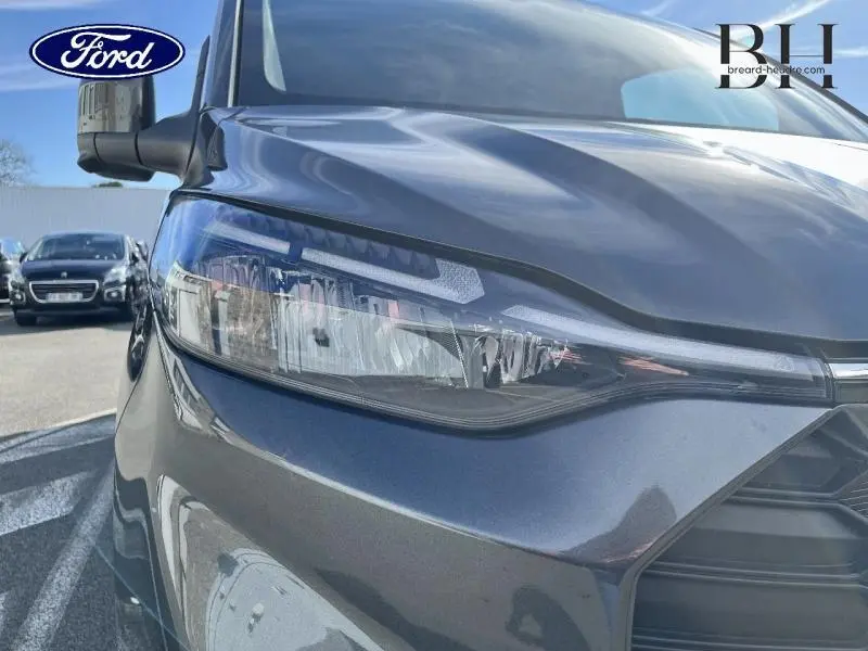 Gros plan sur le phare avant gauche du Ford Transit Custom gris Magnetic métallisé sous lumière naturelle.