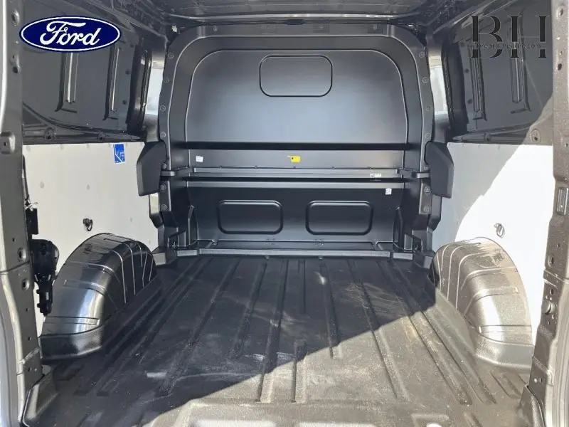 Vue intérieure arrière du fourgon Ford Transit Custom gris, montrant l’espace de chargement vide avec cloison pleine noire.