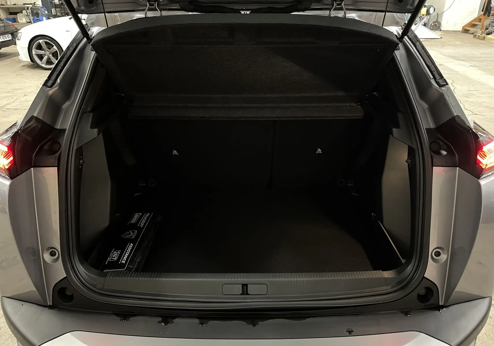 Coffre ouvert vu de l'arrière d'un Peugeot 2008 gris Artense Métal, avec espace de chargement vide et trousse d'assistance.