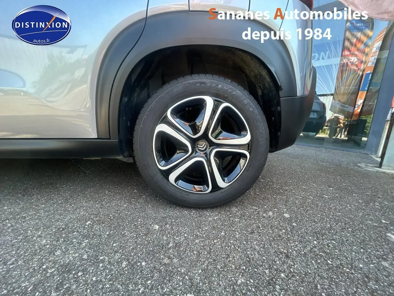 Gros plan sur la roue avant droite du Citroën C3 Aircross gris foncé avec jante 16 pouces bicolore et élargisseur noir mat.