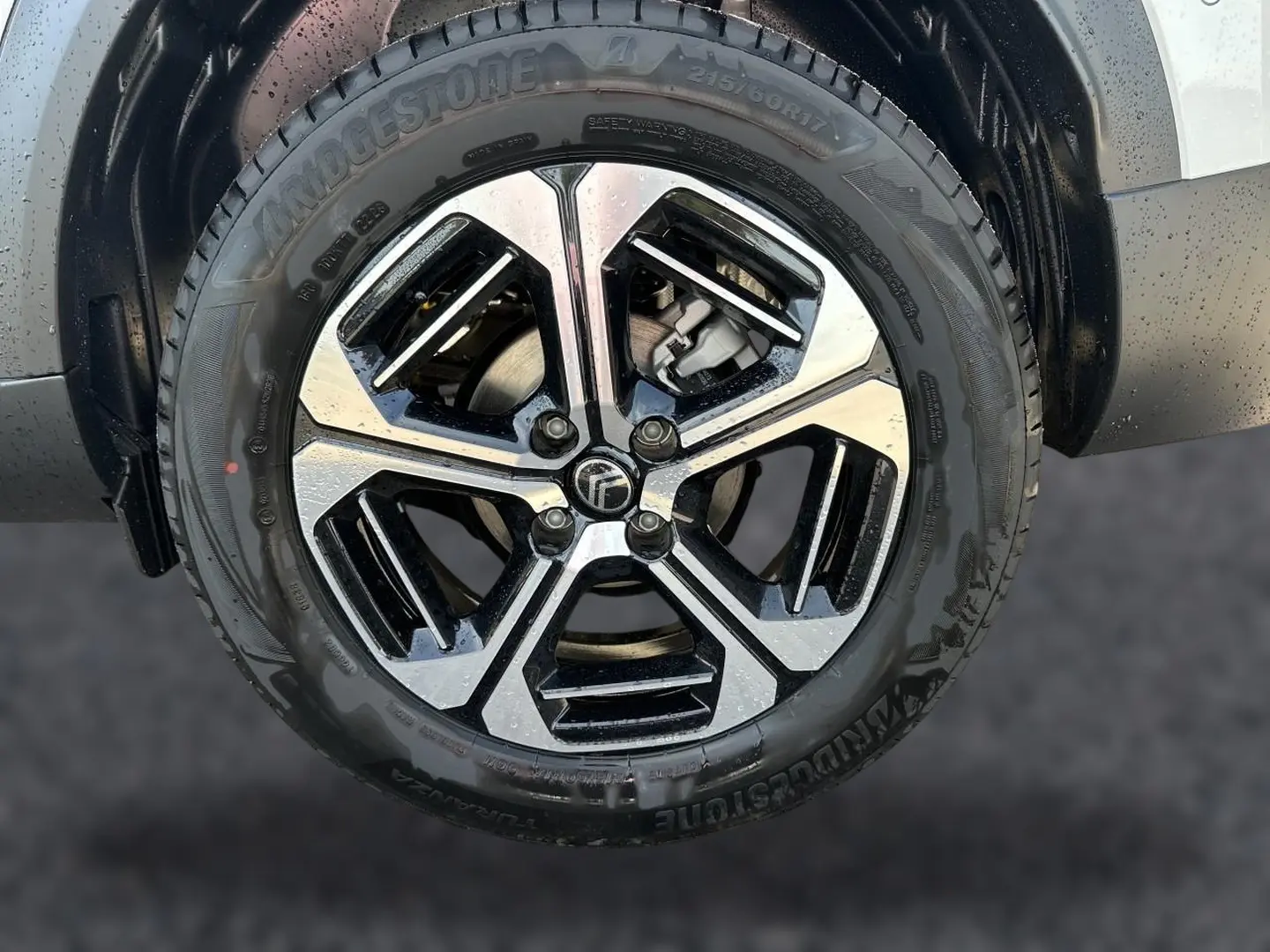 Gros plan sur la jante alu noire et argentée d'un Citroën C3 Aircross blanc, avec pneu Bridgestone humide.