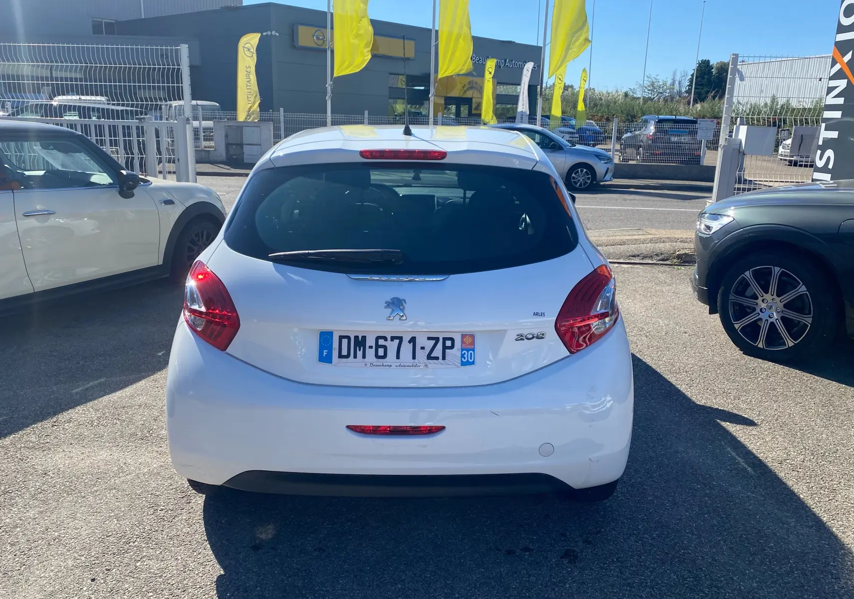 Vue arrière d'une Peugeot 208 blanche de 2014 avec plaques françaises, garée en extérieur sur un parking.